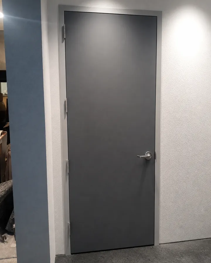 New gray commercial steel door with a lever handle in a finished concrete floored interior