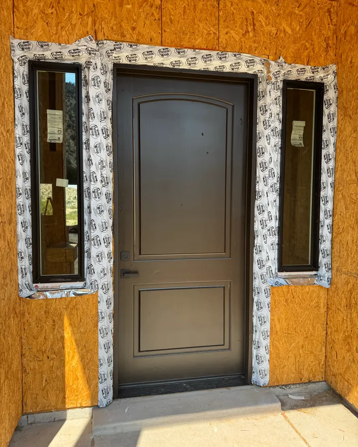 Bronze panel entry door flanked by two sidelight windows, newly installed and still flashed