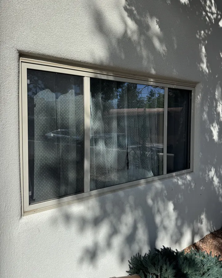 White slider window in a stucco wall under tree shade