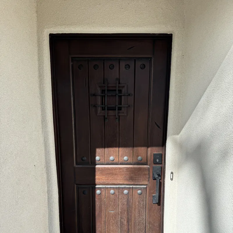 Wood entry door with an iron grille panel, set in a stucco opening